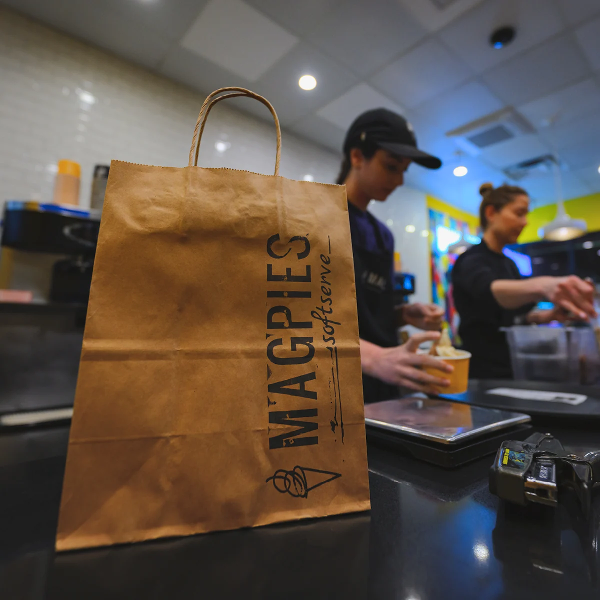 Magpies Softserve takeout bag on the counter while staff prepare an order